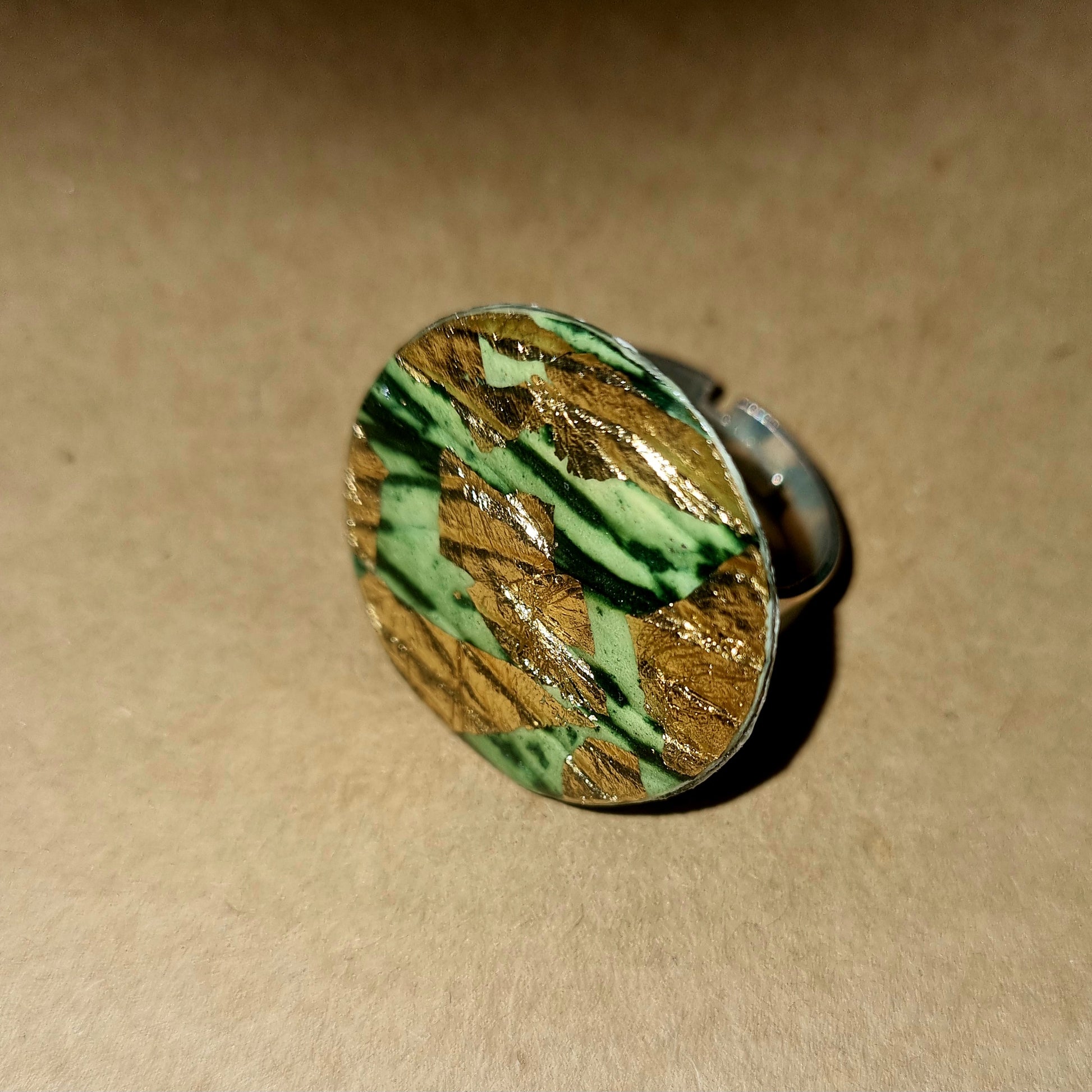 Round ring with green and gold pattern on a beige background